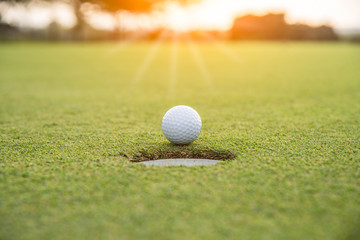 Golf ball putting on green grass near hole golf to win in game at golf course with blur background and sunlight ray