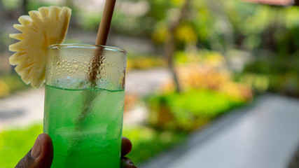 african american hand is holding up a tropical green cocktail while on vacation in Bali its a nice sunny day to have a cool  refreshment while on Vacation 