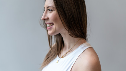 Naklejka premium young beautiful long hair brunette woman smiles flirtatiously by the window light. She laughs from being in good health. she has a bright white teeth and is very happy. wearing athletic clothing