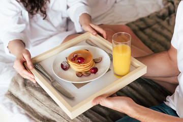 Obraz na płótnie Canvas partial view of couple holding tray with pancakes and glass of orange juice
