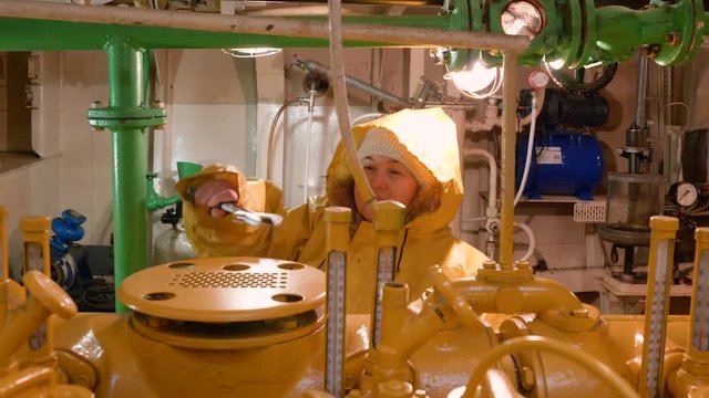 Women repairmen in yellow raincoats inspect engine room in boat in Norway and eliminate breakdowns and shortcomings. Engine room at ship boat. Checking woman