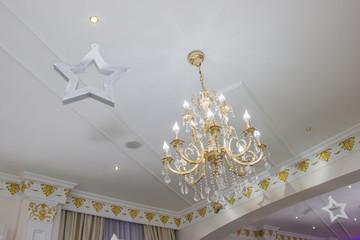 White restaurant ceiling decorated with 3D star made of plastic foam and a big chandelier