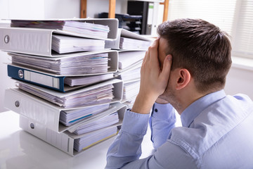 Stressed Businessman In Front Of Stacked Folders