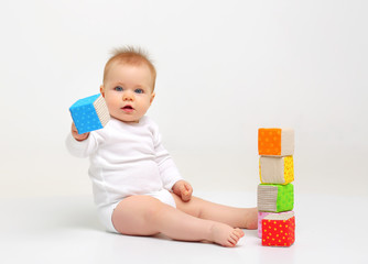 Charming blue-eyed baby sitting on a white background with colored educational toys