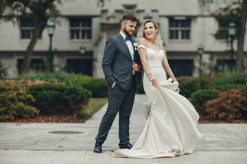 Naklejka premium Beautiful bride in a long white dress. Handsome groom in a black suit. Couple in a summer park
