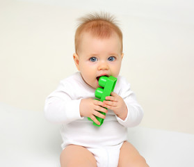 Charming blue-eyed baby sitting on white background and nibbling toys