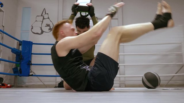 Personal training of professional boxer making adominal exercise with his trainer laying on ringside and lifting his body and legs. Fighter hits partner to stomach of sparrer