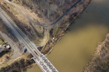Vertical aerial wide angle drone view of  river with a railway bridge, on background forest, village construction site in warm sunny day