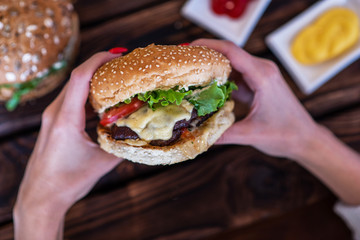 Woman holding cheeseburger. Young girl holding in hands fast food burger, american meal. Beef burger in hands with french fries on rustic wooden board. Selective focus. Toned image with copy space.