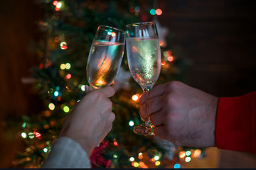 Christmas illuminations and champagne glasses. Hands of people with glasses of champagne, celebrating and toasting in honor of the Christmas and Happy New Year. Couple cheering with champagne flutes.