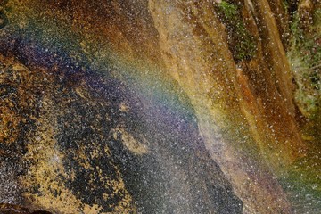 A rainbow is created where water from a waterfall hit the bottom 