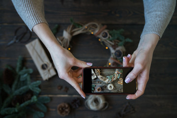 Hands with smart phone pictures of Christmas decoration. Young woman, blogger preparing for the holiday at the home and is making photo at smartphone. Instagram blogger workshop concept. Toned image.