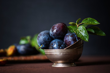 Organic fresh plums in silver vintage bowl on brown surface background. Healthy lifestyle summer vegetarian food. Country garden fruit concept. Beautiful still life. Toned image with copy space.
