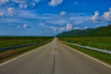 Empty highway leading to the Cameron Highlands, Malaysia. Spectacular view of the hilly terrain in a blue haze and lush tropical rainforest. Asphalt road and beautiful mountain under the blue sky.
