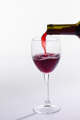 Red wine pouring into glass from bottle on white background