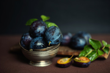 Garden plums on table. Close up of fresh plums with leaves. Summer or autumn harvest of plums. Toned image. Selective focus.