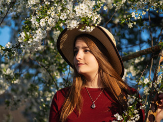 Fashion spring portrait of a woman in a blooming garden. Happy woman in hat