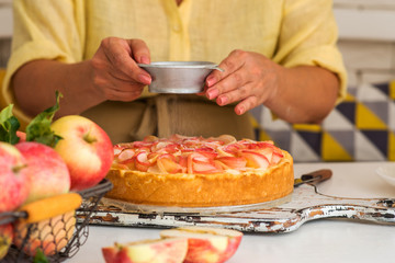 Sweet pastries, powdered sugar, baked apples. Woman is making fruit cake in the kitchen. Ripe red apples in basket.