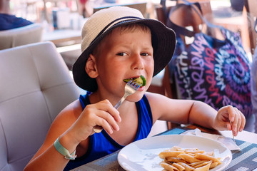a six-year-old child in the hat to eat pasta in a summer Cafe