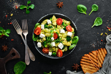 Pasta with spinach, tomatoes and feta cheese. In a black plate on a wooden background Top view. Free space for your text. Flat lay