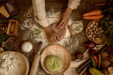 Female hands making fresh homemade pasta. Colored raw vegetable pasta with beets, carrots and spinach. Pasta ingredients and farmers vegetables on the dark wooden table top view.