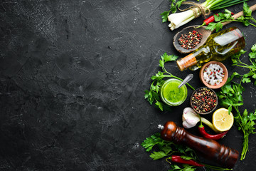 Green parsley sauce, olive oil and spices. Ingredients for chimichurri sauce. On a black background. Top view. free space for your text.