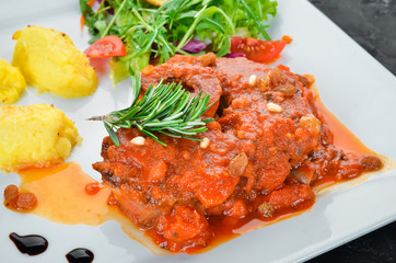 Baked steak on the bone with tomato sauce and potatoes in a plate. Top view. Free space for your text.