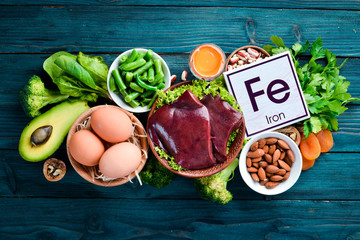 Food containing natural iron. Fe: Liver, avocado, broccoli, spinach, parsley, beans, nuts, on a blue background. Top view. - obrazy, fototapety, plakaty