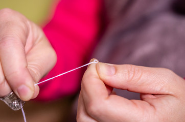 A hand with thimble knotting and cutting a thread on a needle in a sewing session
