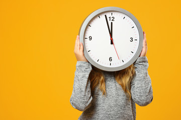 Little child girl holding a big clock on a yellow background. The concept of education, development, school, time management, deadline, time to learn. - obrazy, fototapety, plakaty