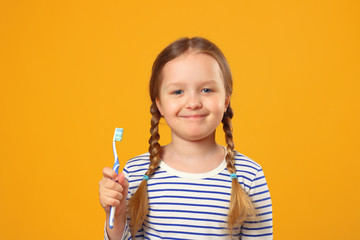 A little child girl in a striped pajamas holding a toothbrush. The concept of daily hygiene. Yellow...