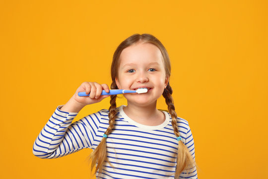 Little child girl in striped pajamas brushing her teeth with a toothbrush. The concept of daily hygiene. Yellow background.