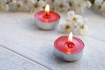 A candle stands on a wooden white table near the branches of white flowers of cherry.