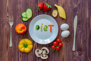 white plate knife fork vegetables, strawberries, two eggs, mushrooms, Apple on wooden background. The inscription vegetables "diet" on a plate