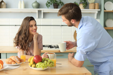 Beautiful young couple in pajamas is looking at each other and smiling while cooking in kitchen at home.