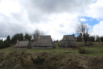 Obraz premium Panoramic view with old rural wooden houses from the beautiful green plateau of Zabljak mountain to the snowy Durmitor mountain