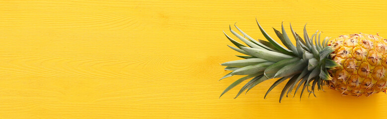 Fototapeta premium Banner of Ripe pineapple over yellow wooden background. Beach and tropical theme. Top view