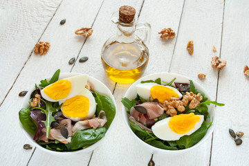 Salad with egg, walnuts and parma ham in white bowls, olive oil in the background
