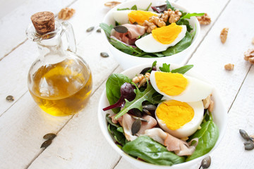 Fototapeta na wymiar Sałatka z jajkiem, orzechami i szynką parmeńska w białych miskach, w tle oliwa z oliwek