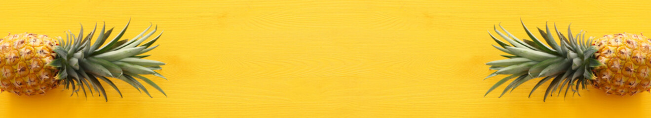 Banner of Ripe pineapple over yellow wooden background. Beach and tropical theme. Top view