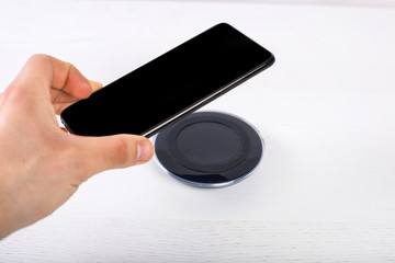 Hand putting mobile phone on wireless charger, modern equipment on white background