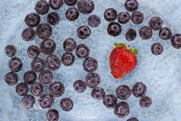 Ripe blueberes and strawberry in blue water with air bubbles