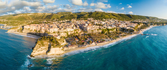 Vista aerea della città costiera di Tropea in Calabria. Affaccio sul mare Mediterraneo delle case colorate, del castello e la spiaggia meta di molti turisti in Estate. Panoramica - obrazy, fototapety, plakaty