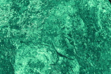 Vintage green background. Rough painted wall of emerald color. Imperfect plane of virid colored. Uneven old decorative toned backdrop of green tint. Texture of emerald hue. Ornamental stony surface.