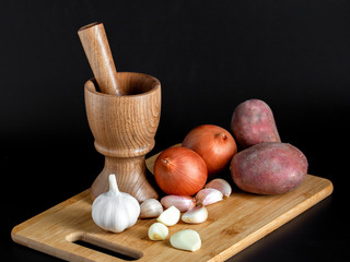 Wooden mortar (pounder), pestle, onion, garlic and other vegetables isolated on black