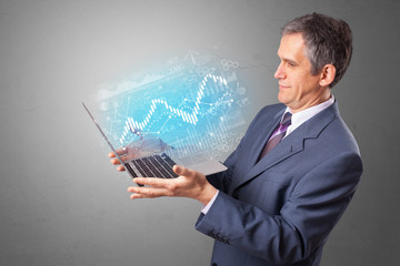 Man holding laptop projecting financial information, diagrams and charts 
