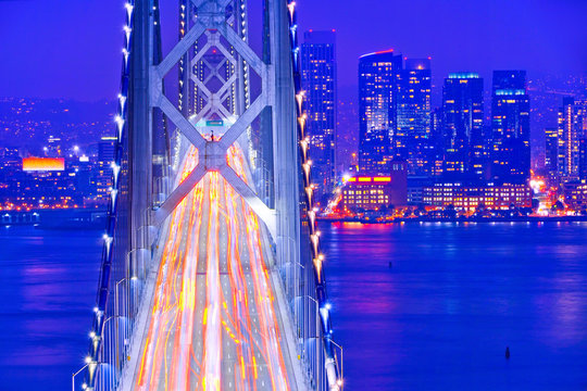 View of Bay Bridge across San Francisco Bay with lots of cars passing through in San Francisco at night.