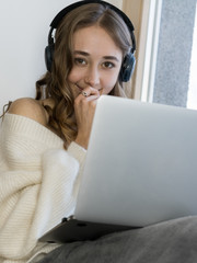 Girl sitting near the window  with laptope, hold big white mag cacao with marshmallow and listen...