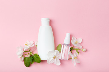 Obraz na płótnie Canvas Face care products (tonic or lotion, serum, spray, micellar water) on pink background with spring apple blossom. Freshness natural anti-age care. Female everyday fresh cosmetics