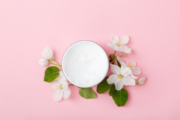 Face or body care cream on pink background with spring apple blossom. Freshness natural anti-age care. Female everyday cosmetics with apple extract. Scrub or anti-cellulite cream